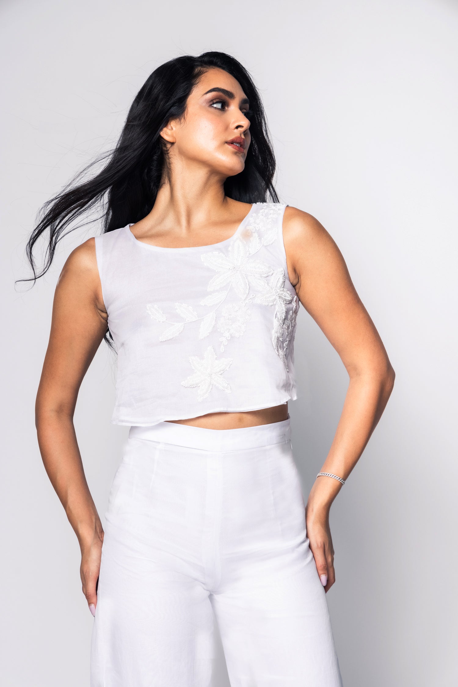 Woman wearing a white sleeveless top and pants against a plain background