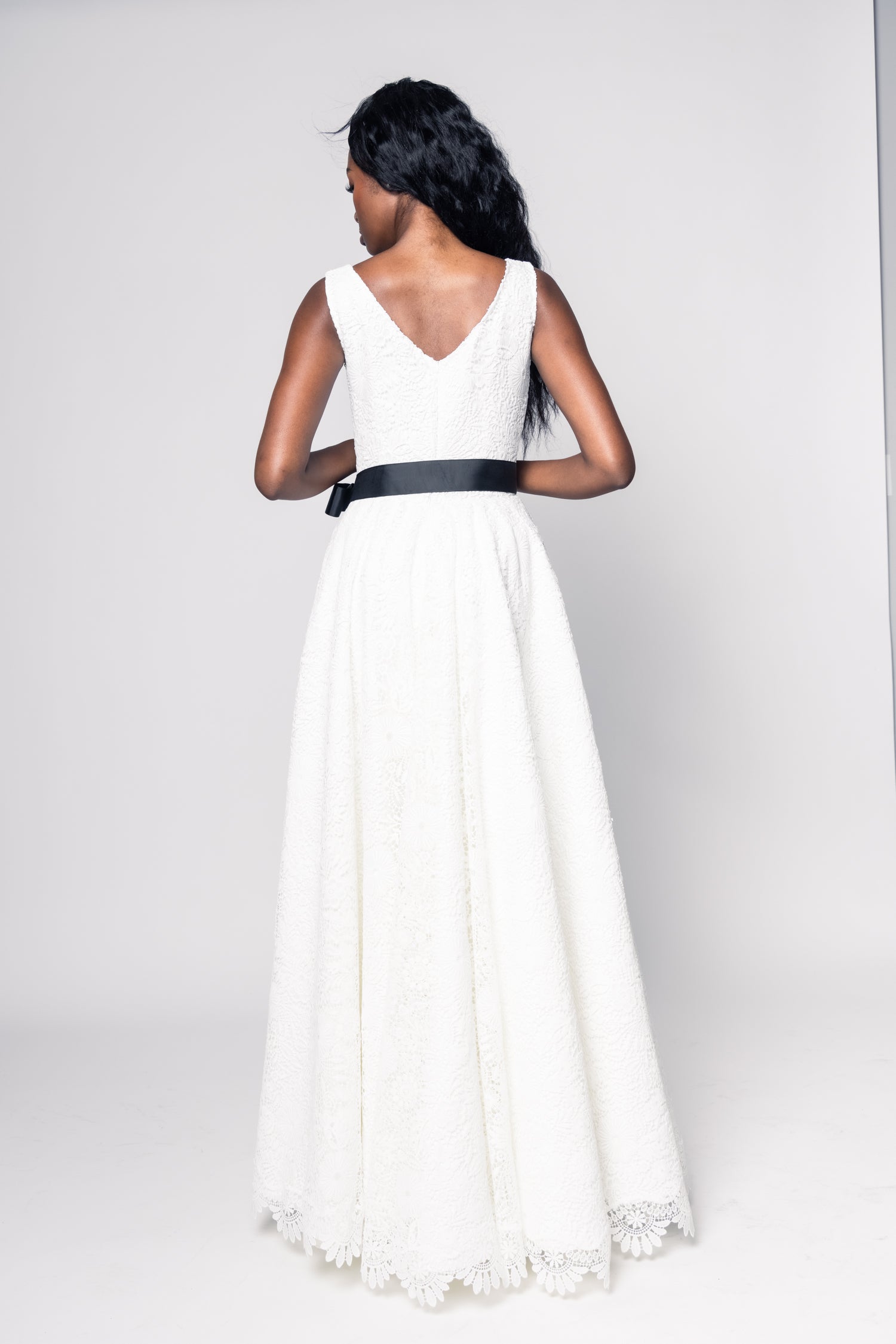 Woman wearing a white dress with a black belt on a plain background