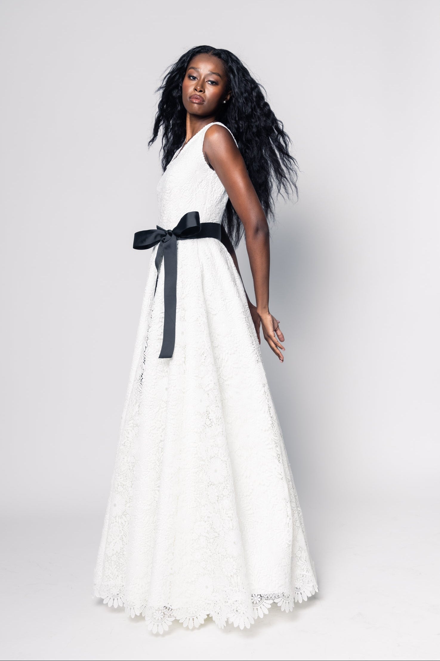 Woman wearing a white dress with a black belt on a plain background