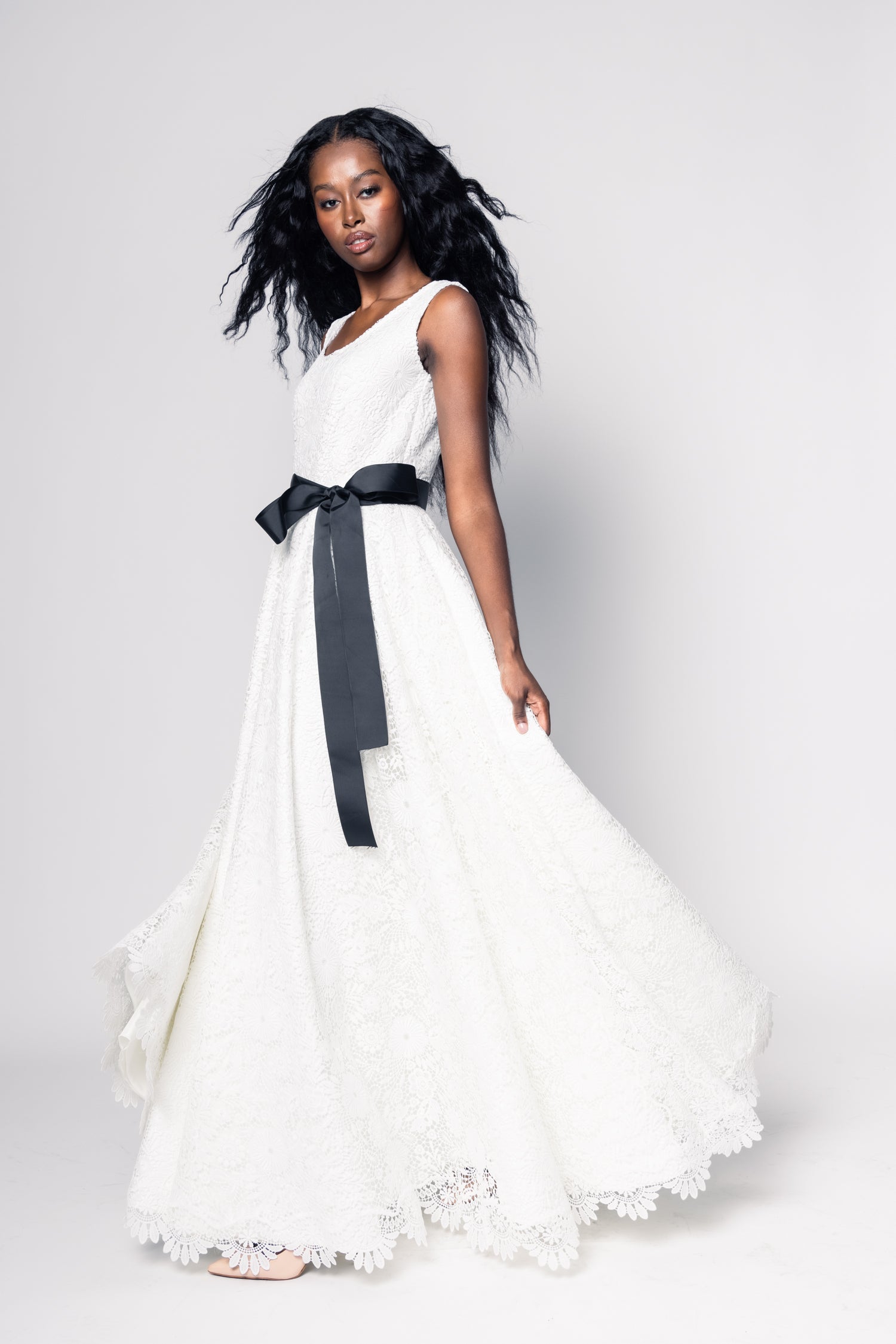 Woman wearing a white dress with a black belt on a plain background