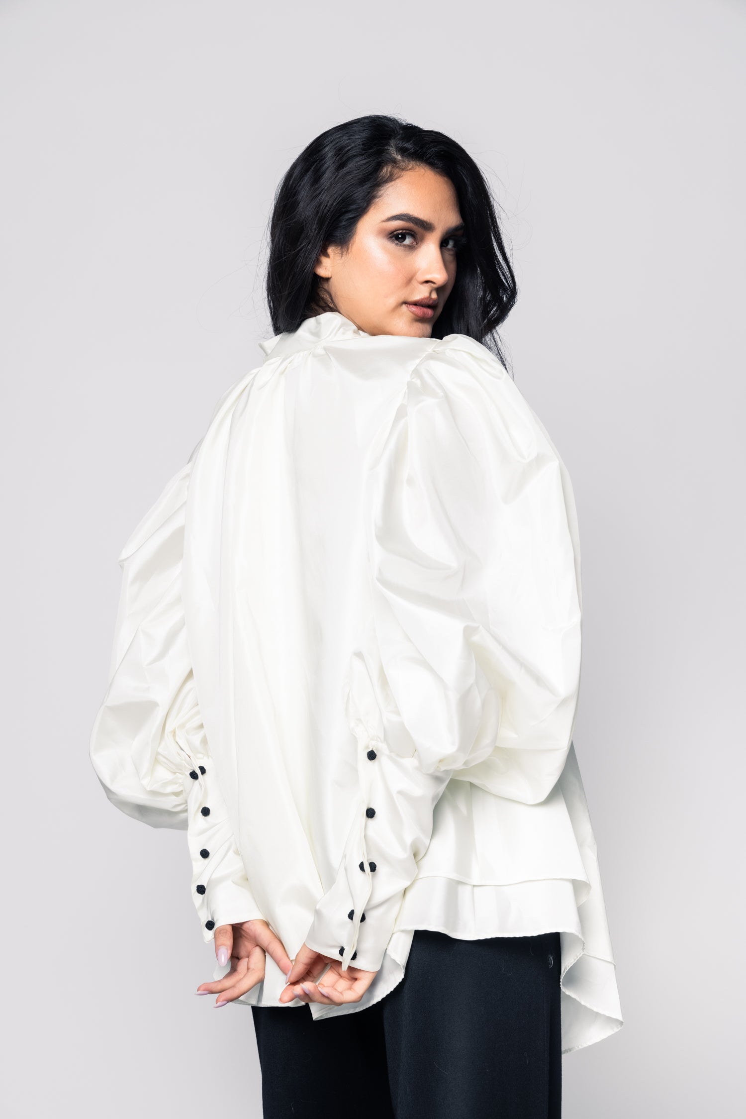 Woman wearing a white blouse with black buttons on a plain background