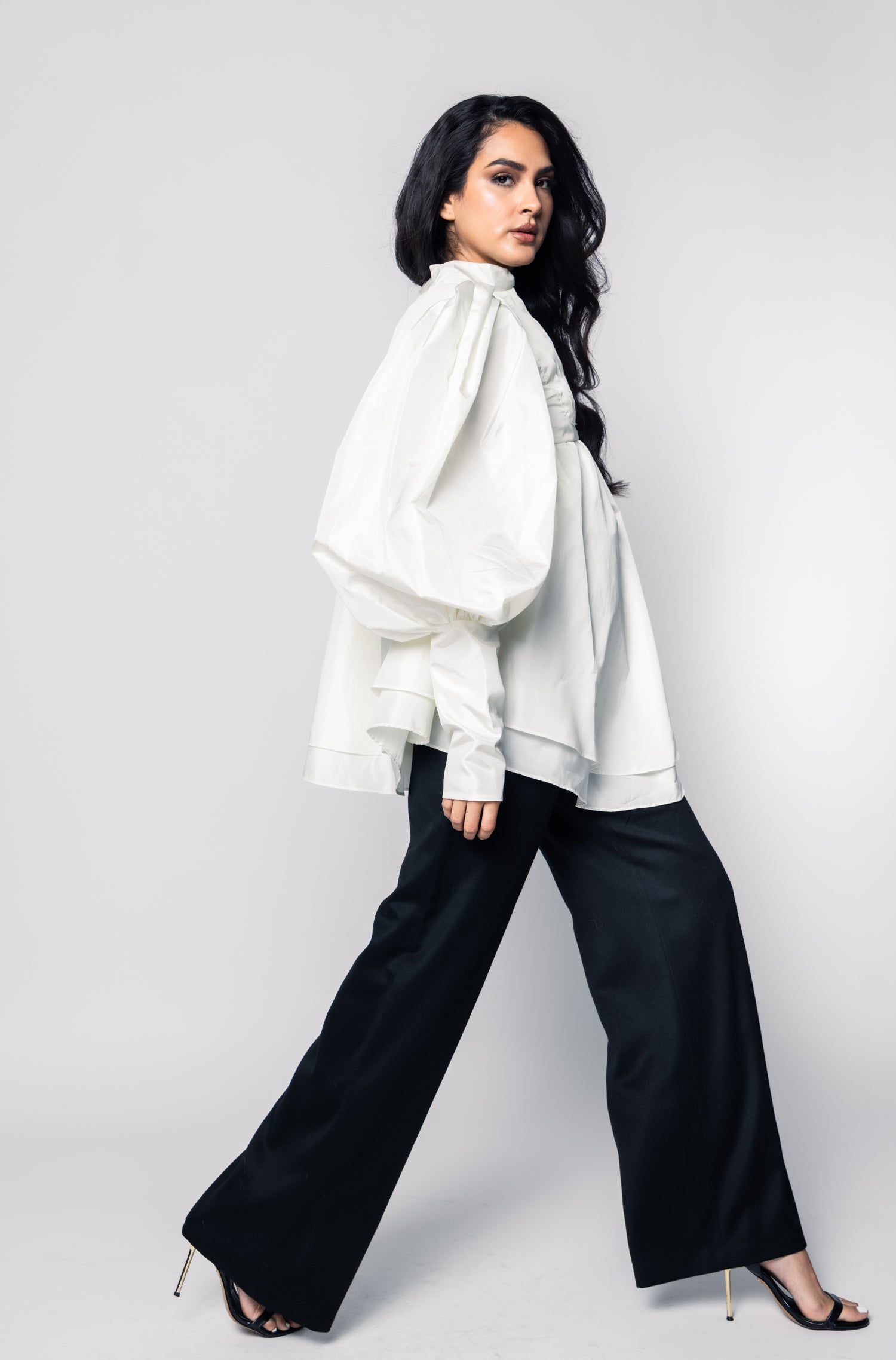 Woman wearing a white blouse and black pants on a plain background