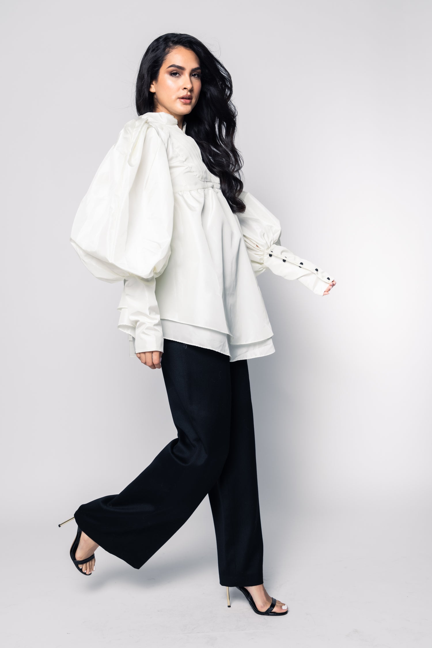 Woman wearing a white blouse and black pants on a plain background