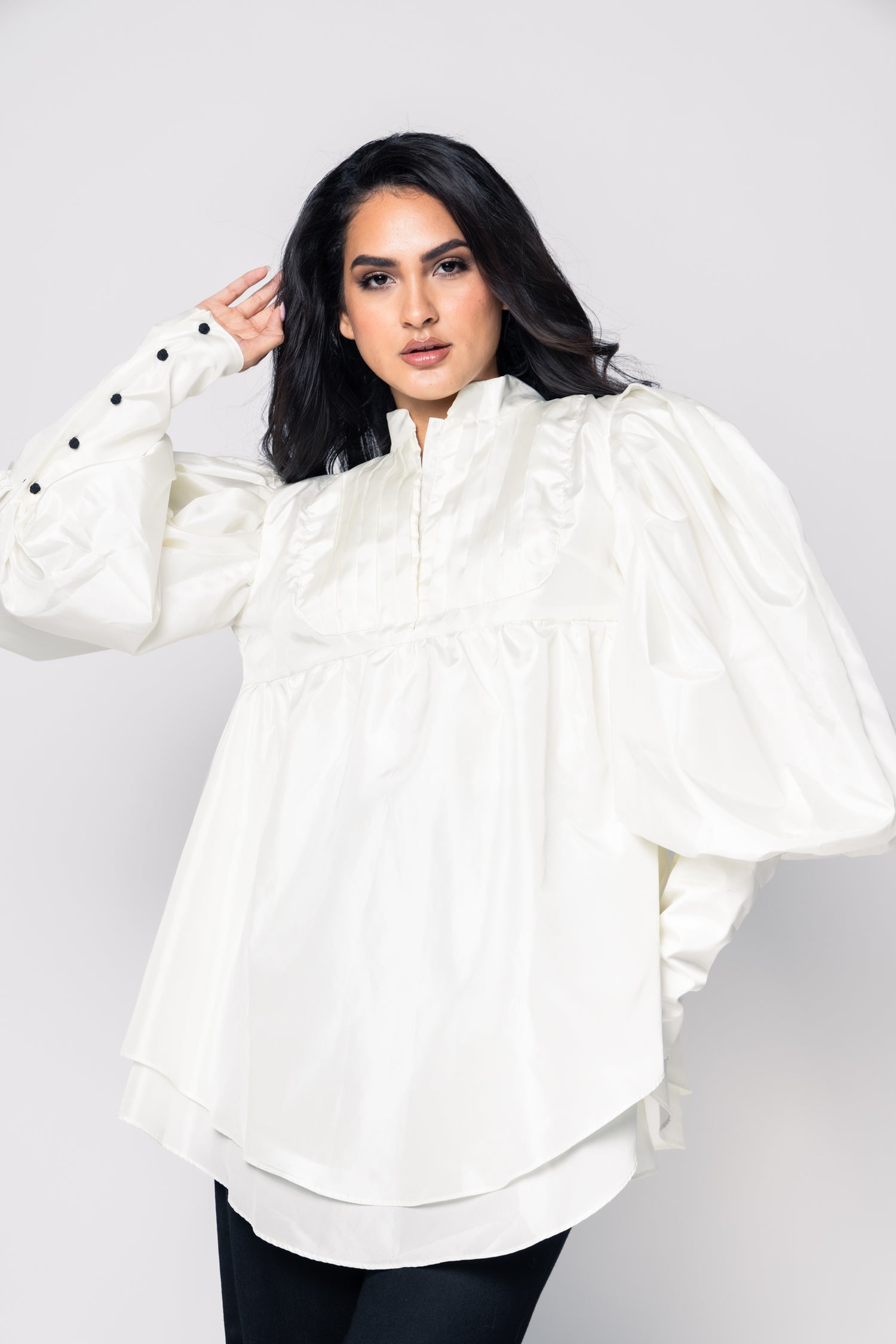 Woman wearing a white blouse with puffed sleeves on a plain background