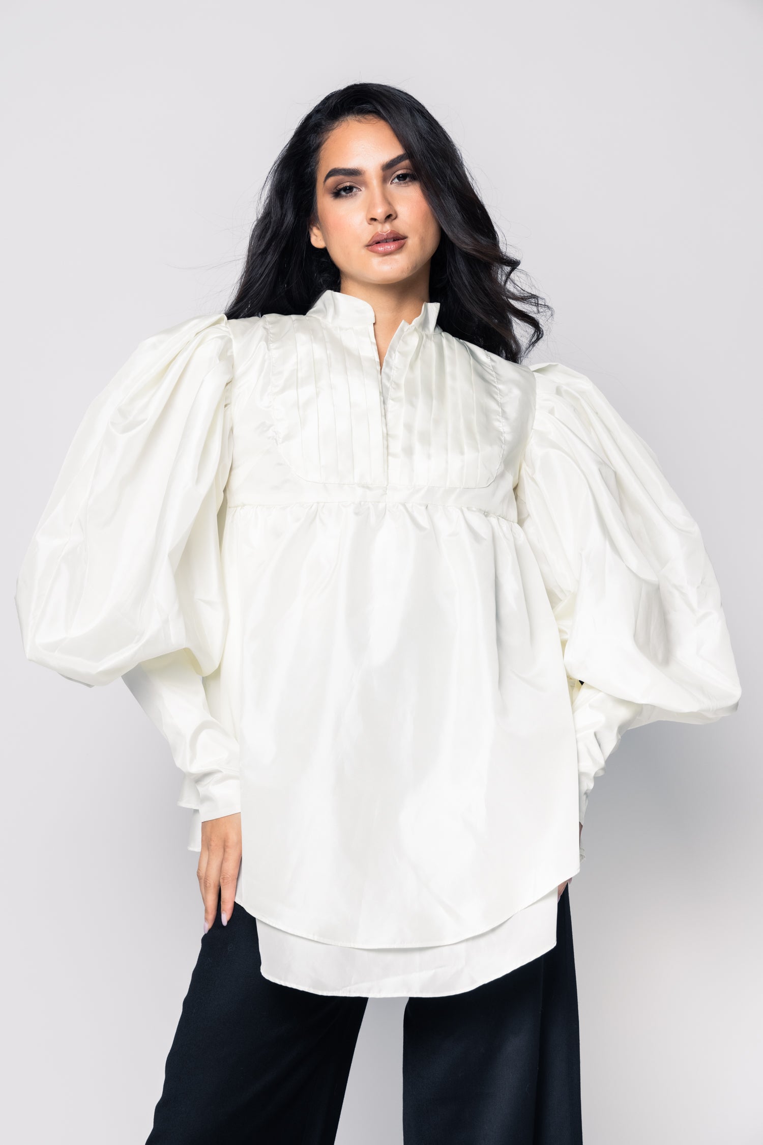 Woman wearing a white blouse with puffed sleeves against a plain background