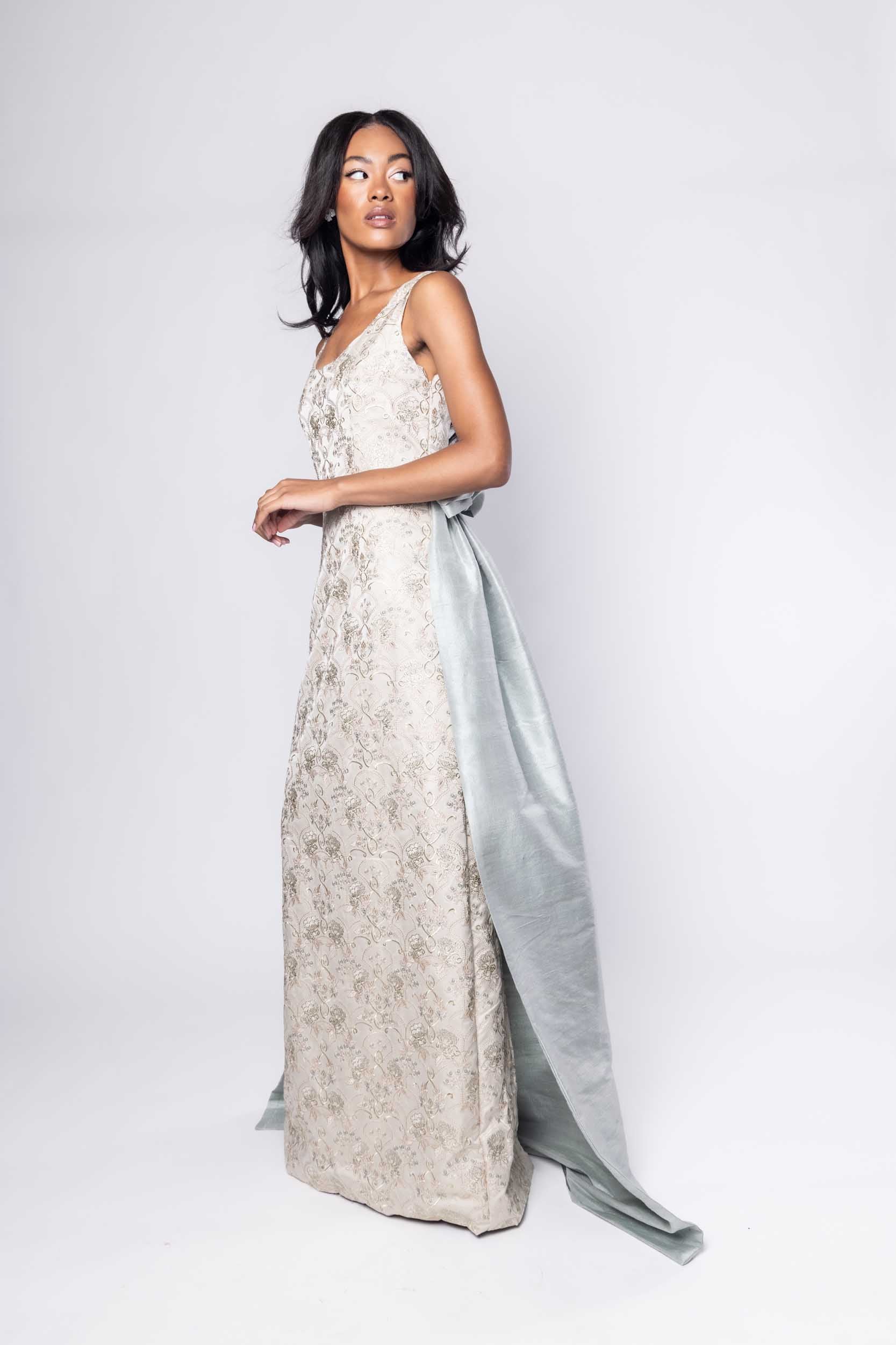 Beautiful model in an embroidered, ornate Sujata Gazder gown with large blue bow train - side view