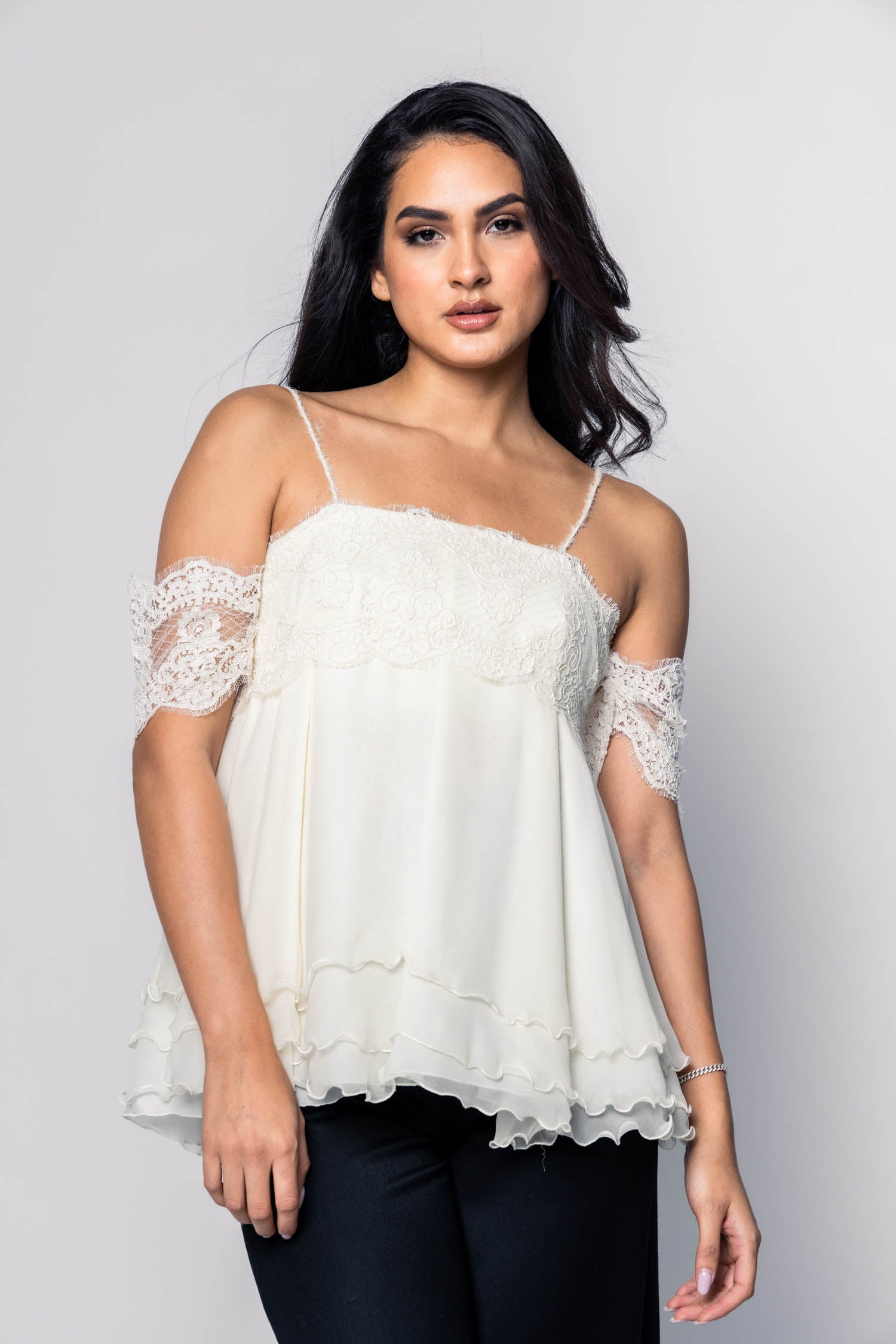 Woman wearing a white lace-trimmed top against a gray background