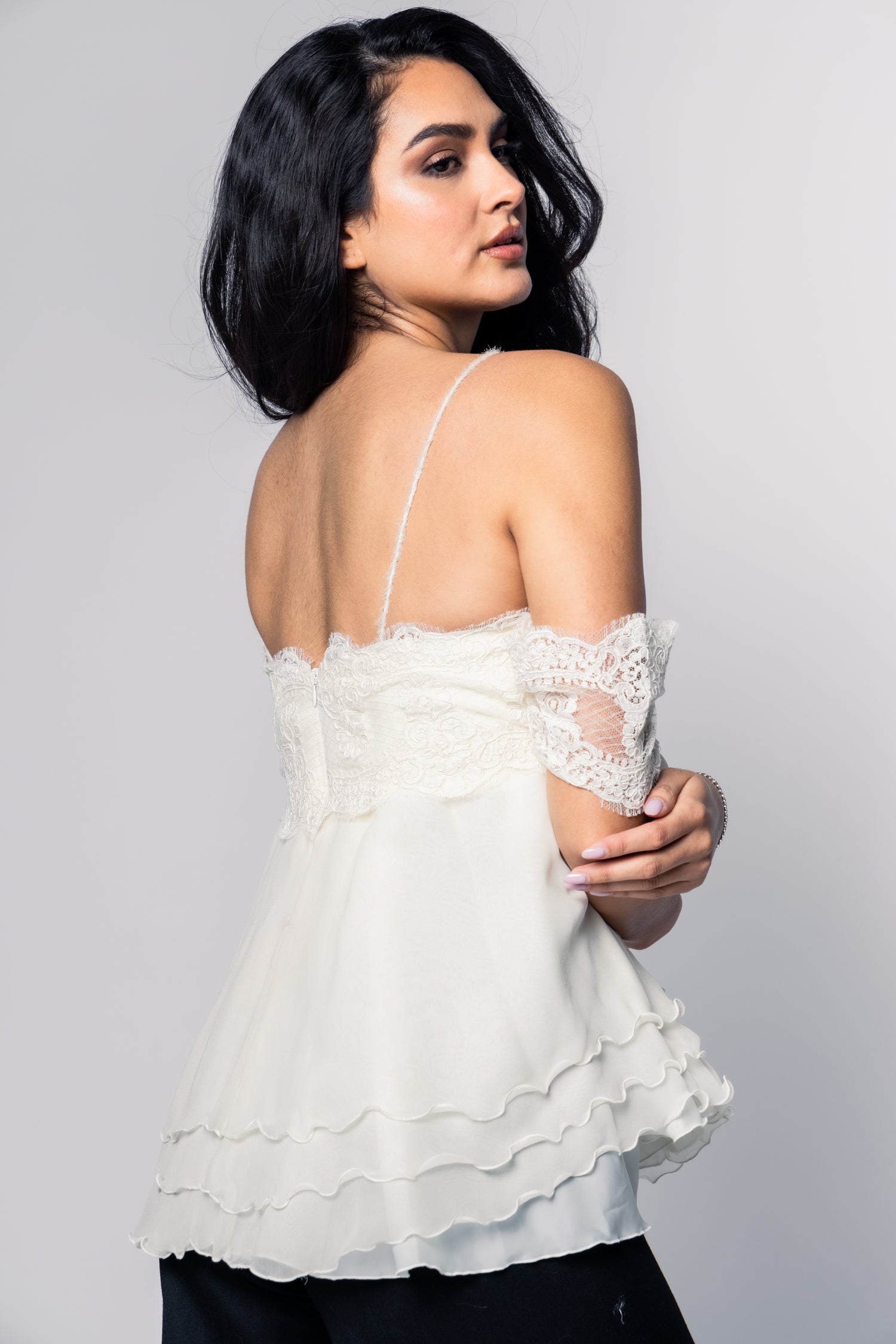 Woman wearing a white lace top against a gray background