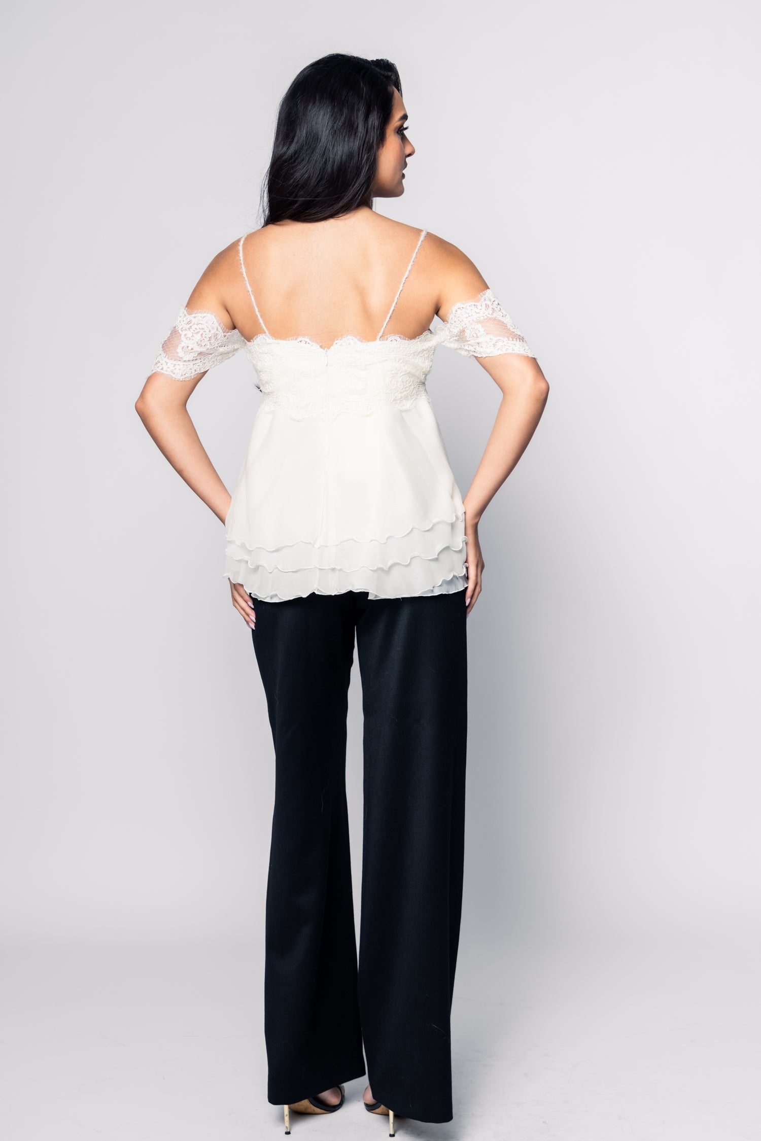 Woman wearing a white top with lace details and black pants on a plain background