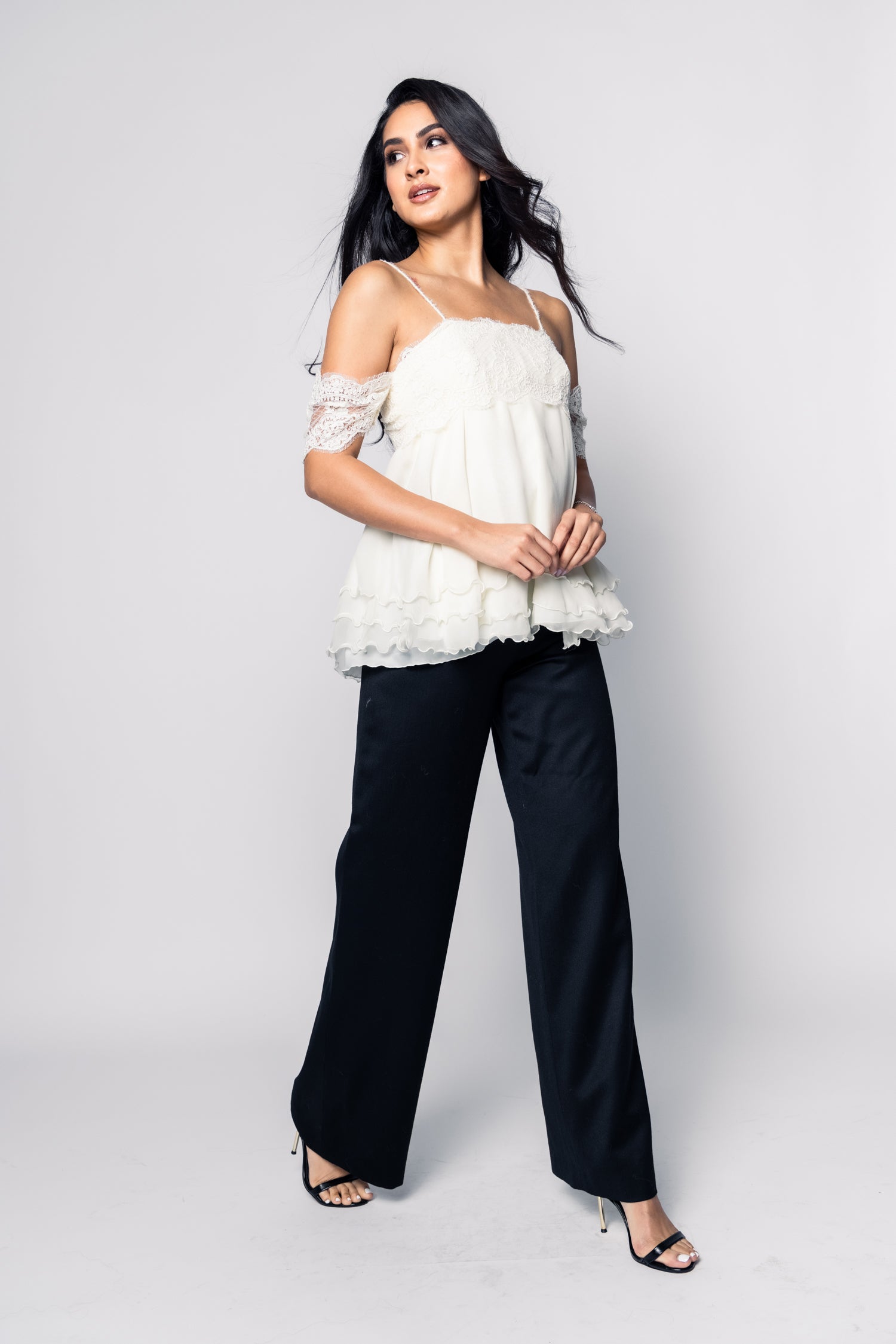 Woman wearing a white lace top and black pants on a white background