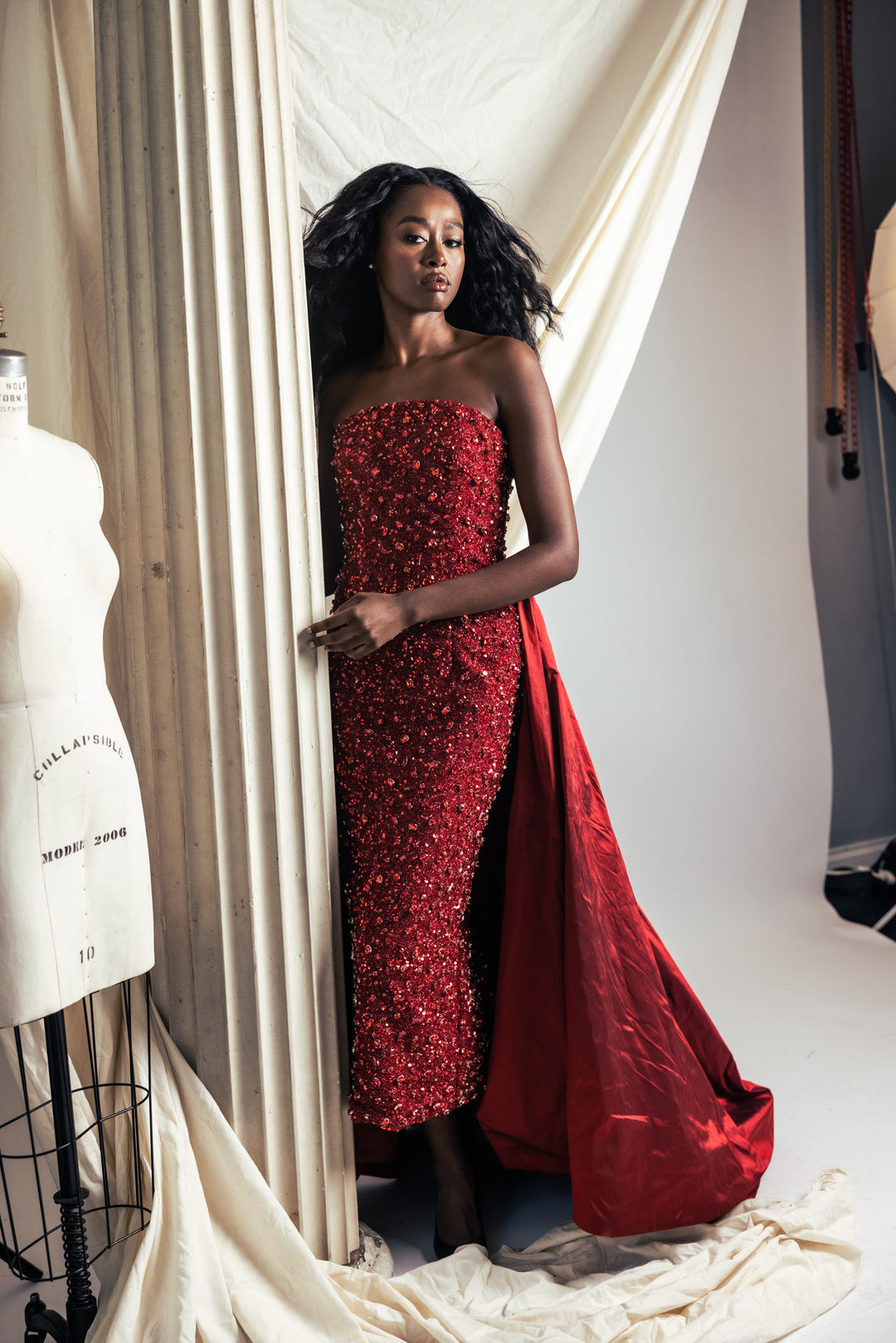Woman in a red strapless gown standing in a studio setting.