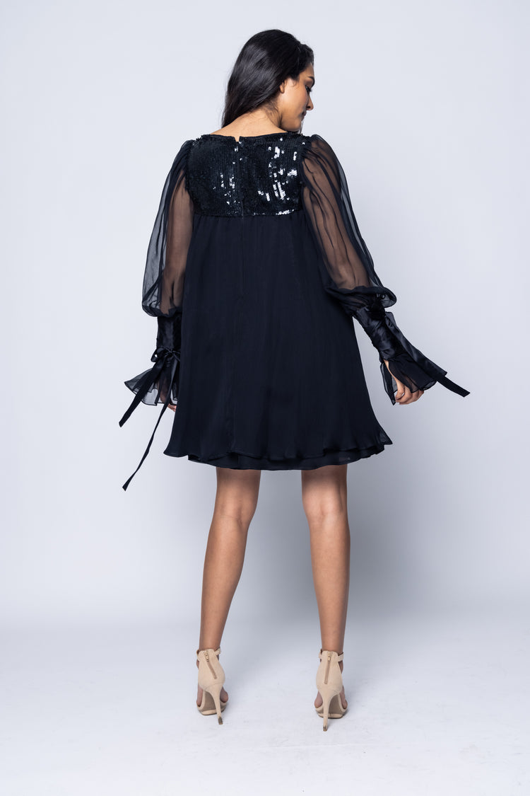 Woman wearing a black dress with sheer sleeves on a white background
