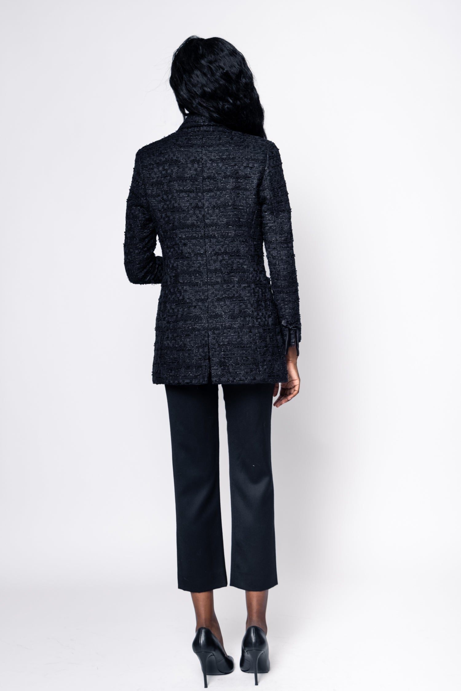 Person wearing a black textured blazer and black pants on a white background