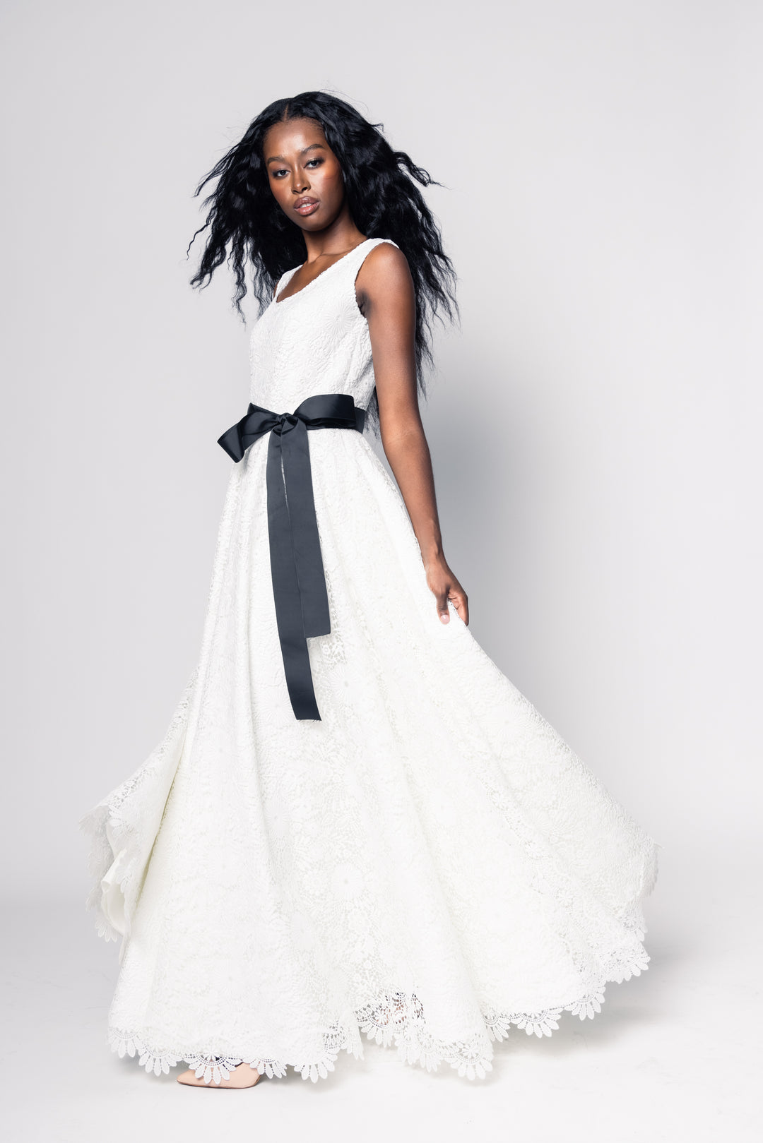 Woman wearing a white dress with a black belt on a plain background