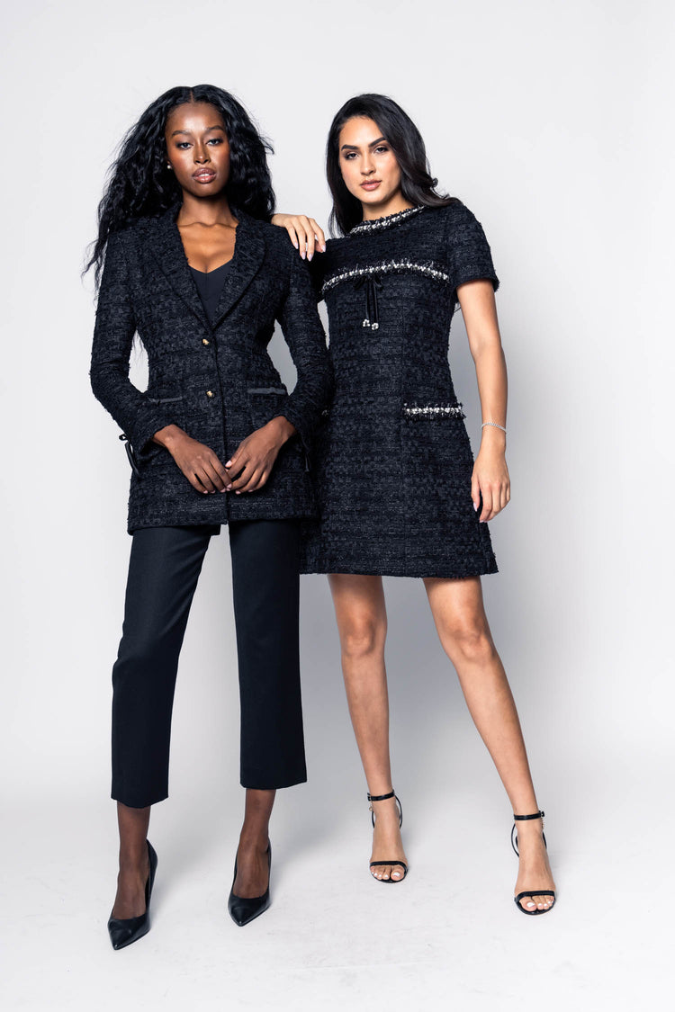 Two women wearing black tweed suit and a boucle short black dress on a white background
