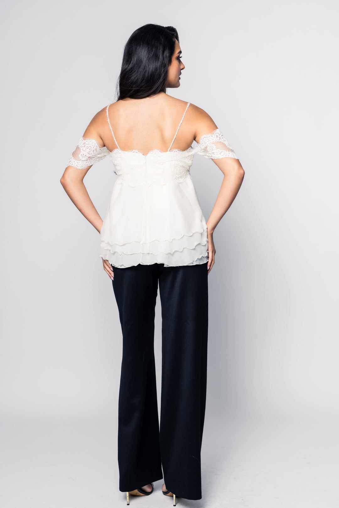 Woman wearing a white top with lace details and black pants on a plain background